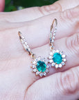Pair of emerald oval cut gemstone earrings with halo diamond on a hand