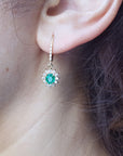 Close-up of a woman wearing a natural oval cut emerald earring, with halo diamond, yellow gold.