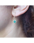Close-up of a woman wearing a natural oval cut emerald earring, with halo diamond, yellow gold.