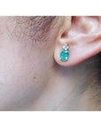 Oval cut natural emerald earrings with three diamonds in 14K white gold on an ear.