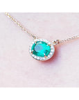 0.90 carat oval Muzo emerald necklace with diamond halo on a 14K yellow gold chain.