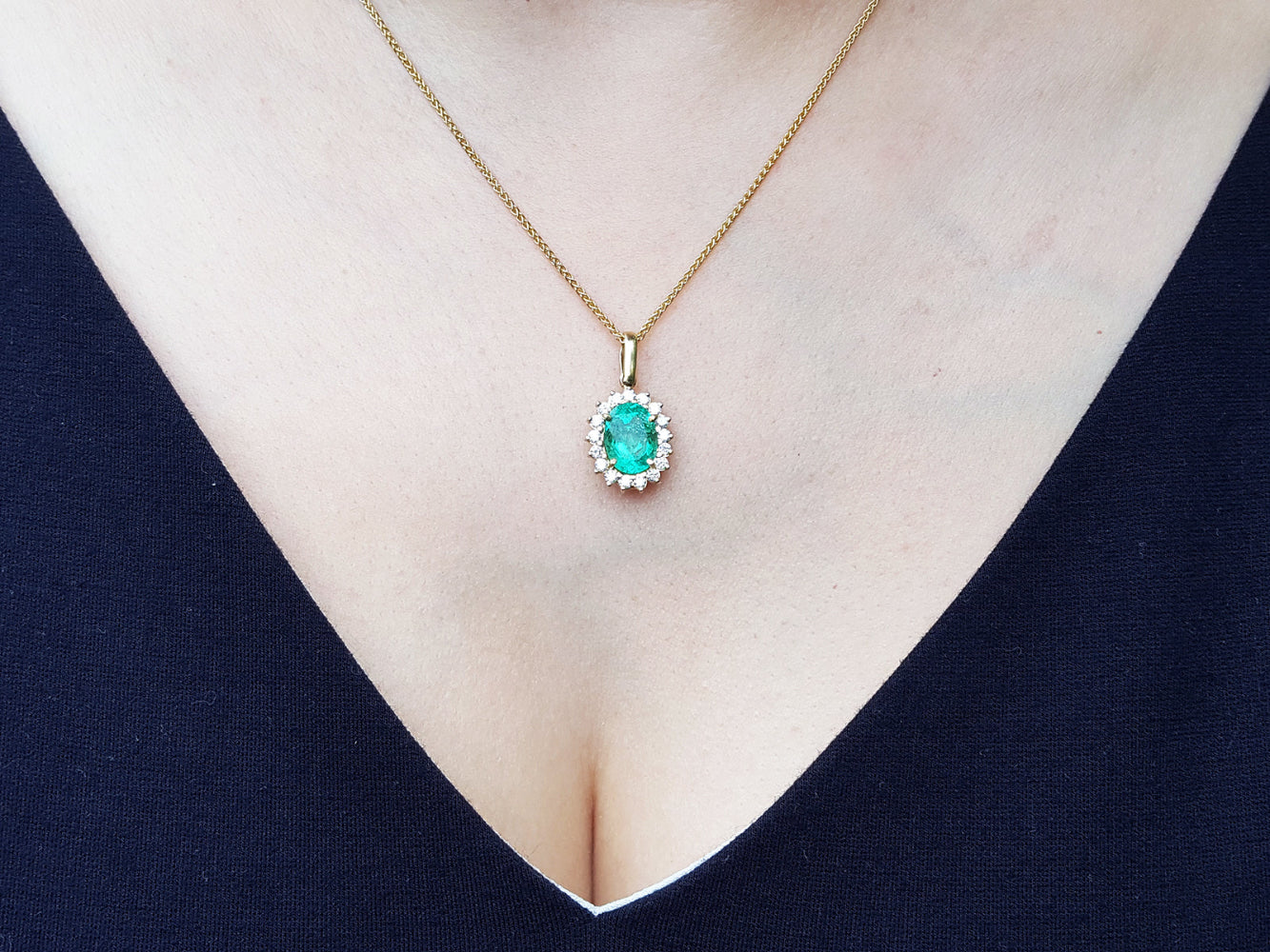 Necklace with a natural oval cut emerald pendant on a person wearing a dark blue top.