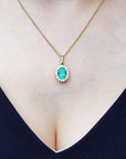 Necklace with a natural oval cut emerald pendant on a person wearing a dark blue top.