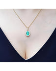 Oval natural emerald pendant with halo diamonds in 18K yellow gold on a woman's décolletage.