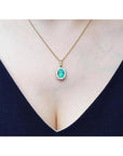 Oval natural emerald pendant with halo diamonds in 18K yellow gold on a woman's décolletage.