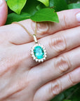 Gold necklace with a natural emerald pendant on a hand against a green leafy background.