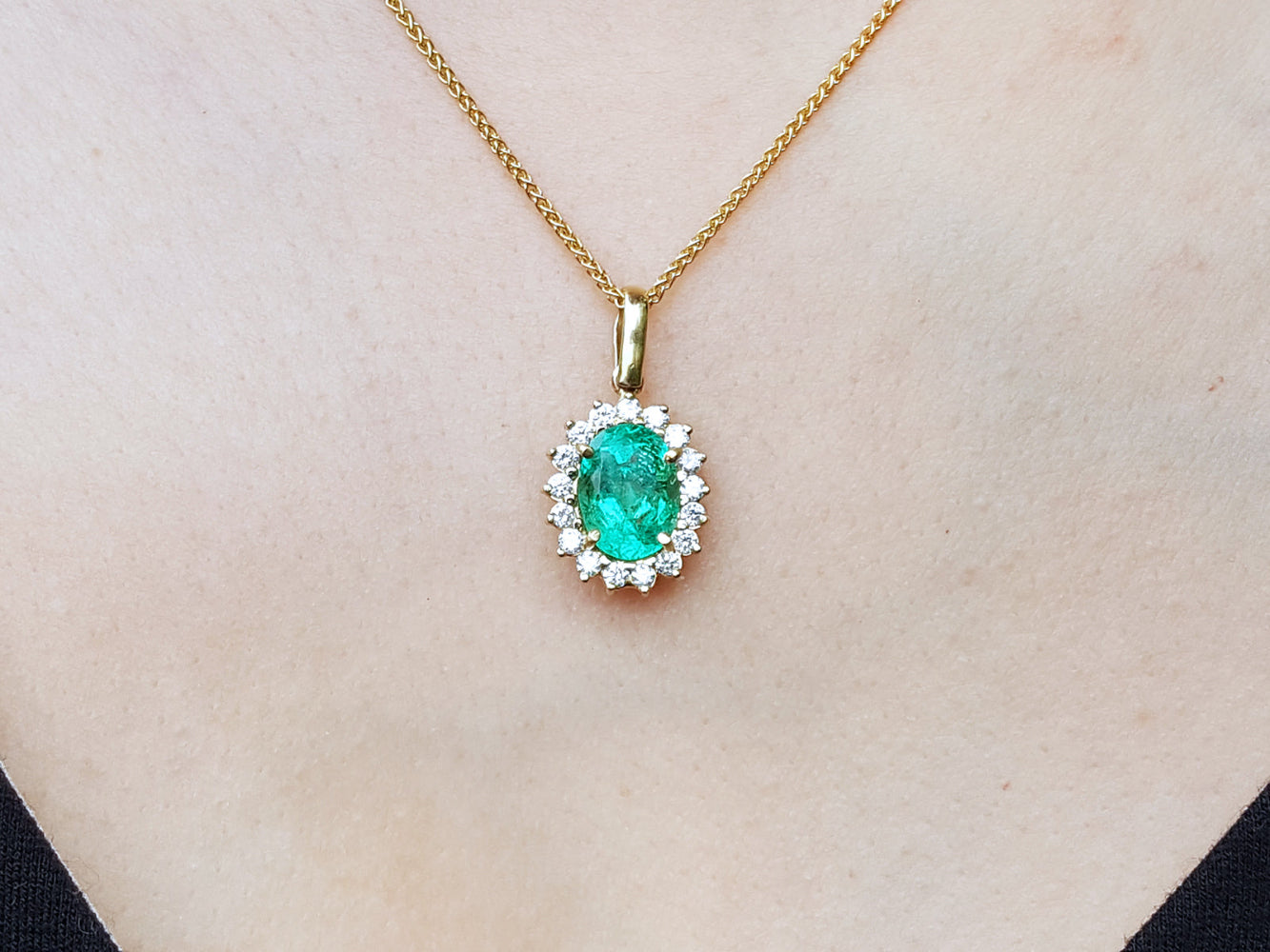 Gold necklace with an oval cut emerald pendant on a plain background.