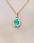 Gold necklace with an oval cut emerald pendant on a plain background.