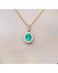 Oval 3.01 ct natural emerald pendant with halo diamonds on an 18K yellow gold chain.