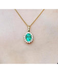 Oval 3.01 ct natural emerald pendant with halo diamonds on an 18K yellow gold chain.