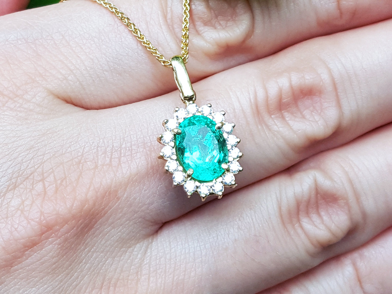 Gold necklace with a natural oval emerald pendant held in a hand.