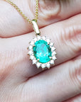 Gold necklace with a natural oval emerald pendant held in a hand.