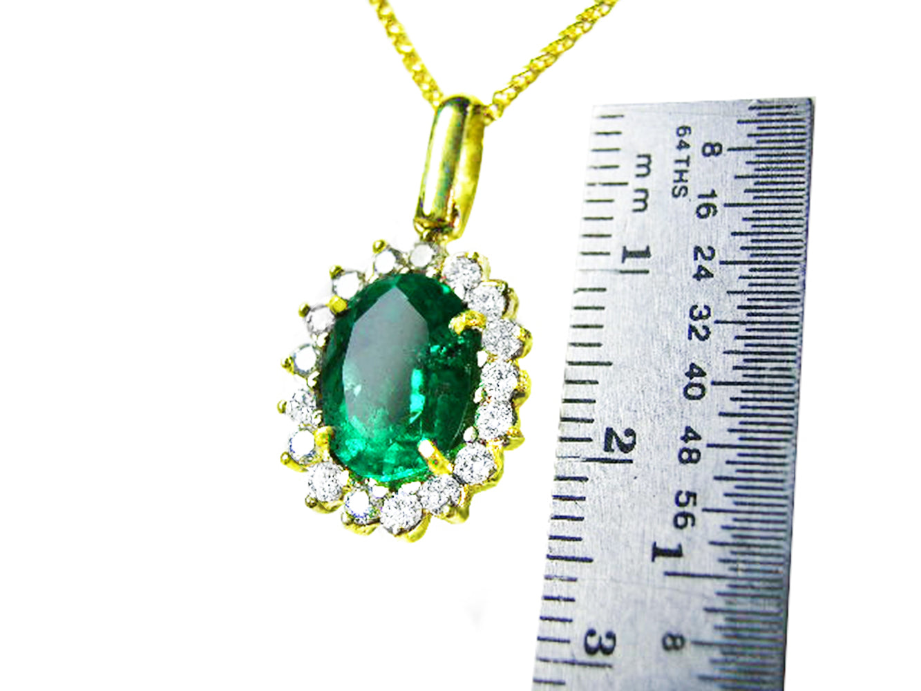 Gold pendant with an oval cut emerald and diamonds next to a ruler for scale on a white background.