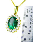 Gold pendant with an oval cut emerald and diamonds next to a ruler for scale on a white background.