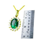 Oval natural emerald pendant with halo diamonds in 18K yellow gold, shown with a ruler for scale.