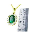 Oval natural emerald pendant with halo diamonds in 18K yellow gold, shown with a ruler for scale.