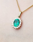 Gold necklace with an oval cut natural emerald necklace pendant on a light pink background.