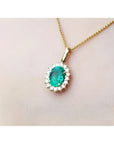 Gold necklace with an oval cut natural emerald necklace pendant on a light pink background.
