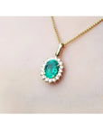 Gold necklace with an oval cut natural emerald necklace pendant on a light pink background.