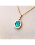 Gold necklace with an oval cut natural emerald necklace pendant on a light pink background.