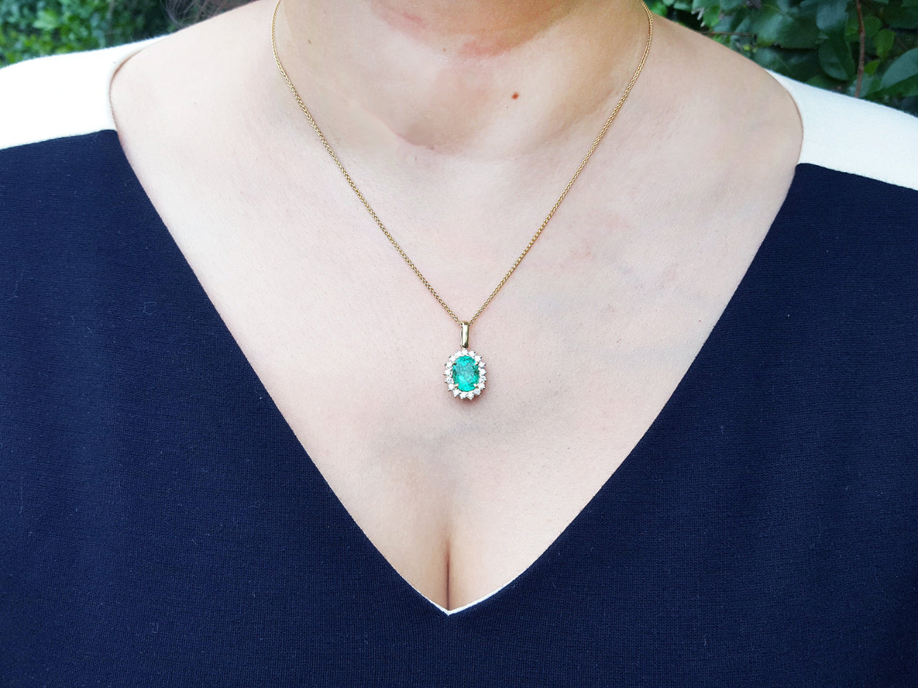 A woman wearing a necklace with an oval emerald pendant on a dark blue top.