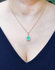 A woman wearing a necklace with an oval emerald pendant on a dark blue top.