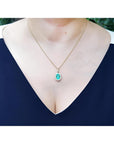 Oval natural emerald pendant with halo diamonds in 18K yellow gold, worn on a woman's neck.