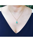 Oval natural emerald pendant with halo diamonds in 18K yellow gold, worn on a woman's neck.