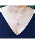 Oval natural emerald pendant with halo diamonds in 18K yellow gold, worn on a woman's neck.