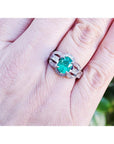 Oval emerald ring in 18K white gold with a decorative diamond band on a hand.