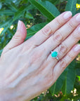 Hand wearing an oval emerald ring with leaves in the background,
