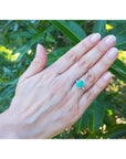 Hand wearing an oval emerald ring with leaves in the background,