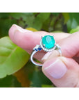 14K white gold halo ring with a deep green oval emerald and diamond accents.