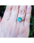 Oval-cut 2.02 ct. deep green emerald halo ring with diamonds on a 14K white gold band, worn on a hand.