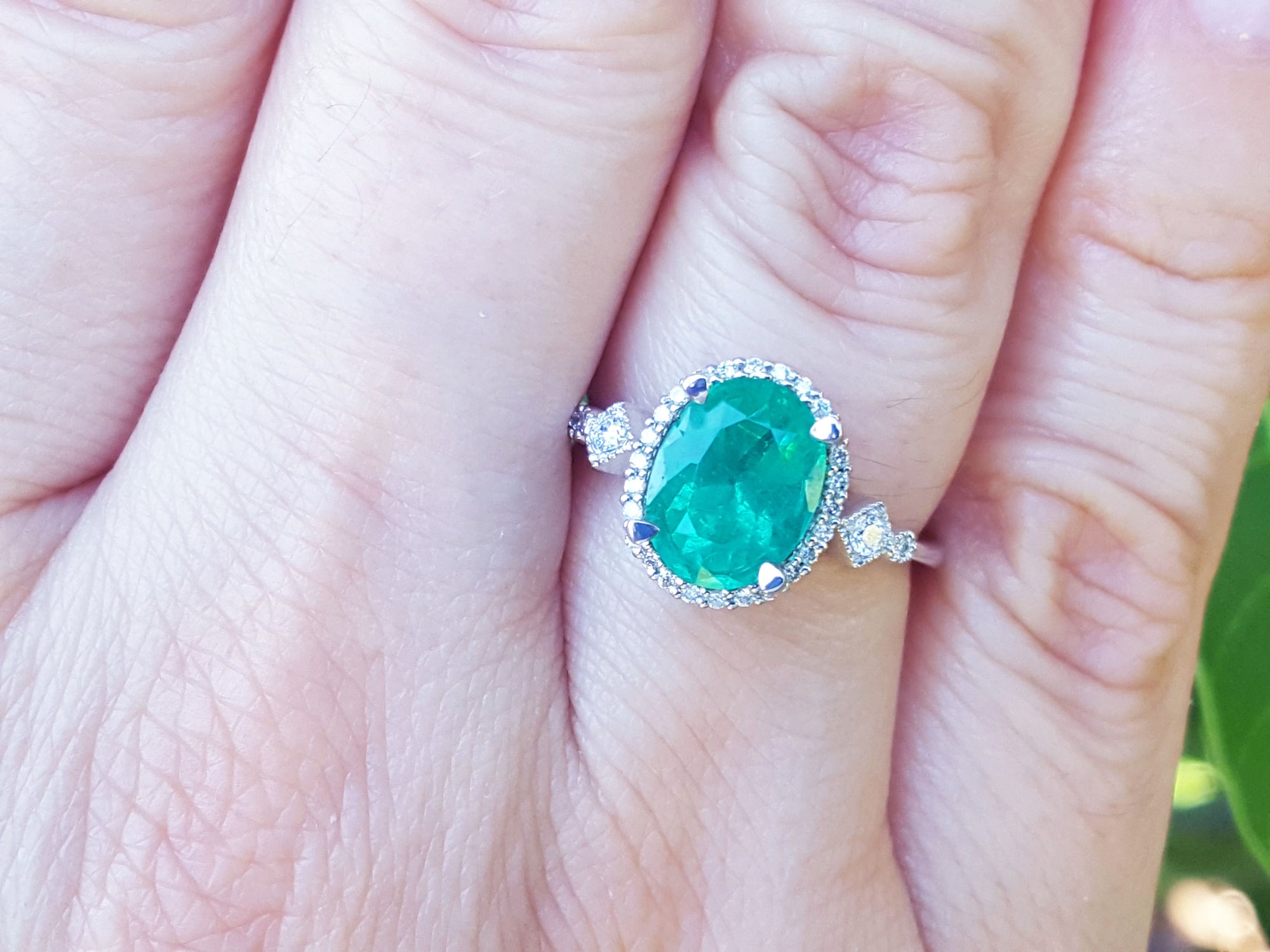Ring with a natural emerald oval cut and accent diamonds on a person's finger.