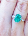 Ring with a natural emerald oval cut and accent diamonds on a person's finger.