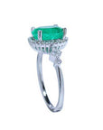 An emerald ring displaying the top side gallery and band with accent diamonds.