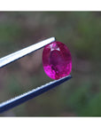 Ruby gemstone held by tweezers with a blurred green background