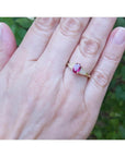Genuine oval cut Burmese ruby ring with side diamonds set in 14k yellow gold on a woman's finger.