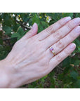Woman's hand wearing a 14k yellow gold ring with a deep red oval ruby and side diamonds.