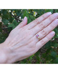 Woman's hand wearing a 14k yellow gold ring with a deep red oval ruby and side diamonds.