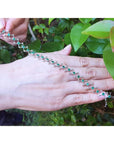 14K white gold bracelet with round Colombian emeralds in bezel-set, diamond-shaped links on a woman's hand.