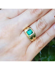 1.53 ct. square emerald solitaire ring in a yellow gold bezel setting on a hand.