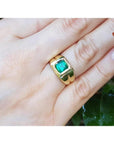 1.53 ct. square emerald solitaire ring in a yellow gold bezel setting on a hand.