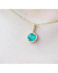 Gold necklace with a round cut natural emerald pendant on a person's neck.