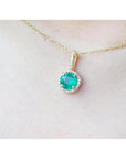 Gold necklace with a round cut natural emerald pendant on a person's neck.