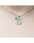 Necklace with a dolphin pendant with emerald and diamonds on a person's neck.