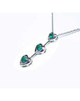 14K white gold heart journey pendant necklace with three round Colombian emeralds.