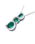 14K white gold journey pendant with three round-cut Colombian emeralds and diamond accents on a chain.