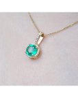 Gold necklace with a round cut natural colombian emerald pendant on a light pink skin background,